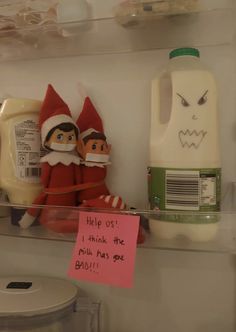 two elf dolls sitting on top of a shelf next to a bottle of yogurt