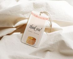 a tag that says thank you next to some pancakes on a white bed linens