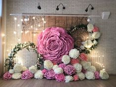 large pink and white flowers are arranged in front of a brick wall with lights on it