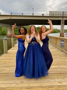 three women in dresses standing on a dock with their hands up to the camera and smiling