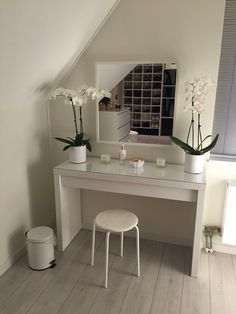 a white vanity table with flowers on it and a stool in front of the mirror