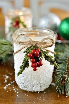 a mason jar filled with snow and holly wreaths on top of a wooden table