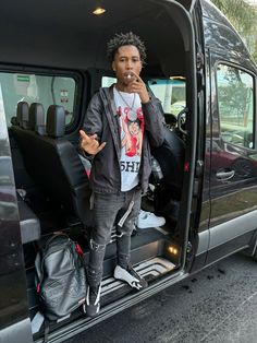 a young man standing in the back of a van with his hand up to his mouth