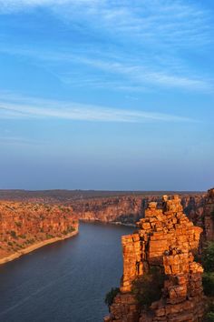 a river running through a canyon next to a rocky cliff side under a blue sky with wispy clouds