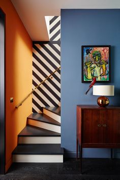 a painting hangs on the wall next to a stair case with a lamp and table