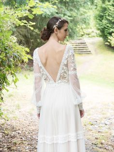 a woman in a white dress is walking through the woods with her back to the camera