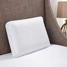 a close up of a pillow on a bed with a lamp in the corner behind it