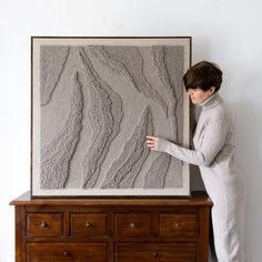 a woman standing next to a painting on top of a dresser