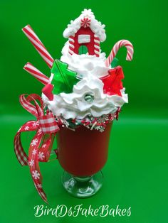 Red Holiday Sundae. Fake Bake, Faux Sundae This cheery sundae starts with a glass pedestal mug which is red inside. It is topped with a mountain of faux whipped cream with an adorable gingerbread house on top. The faux whipped cream is adorned with straws,faux marshmallows, a candy cane, Christmas trees, chocolate chips, peppermints and a mini lollipop. The rim of the glass has white dripping loaded with holiday faux sprinkles. Attached to the handle are a red gingham and snowflake ribbons. This mug will make anyone on your Christmas list smile. It is the perfect gift! *Not edible* *display items not included* *approximate measurements are 4.5 inches wide by 9.5 inches tall* Faux Marshmallows, Fake Gifts, Fake Food Props, Candy Cane Christmas, Food Props, Glass Pedestal