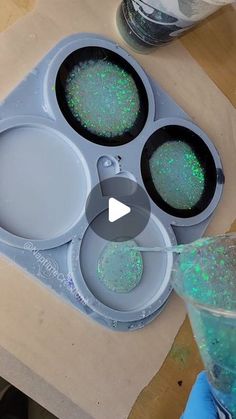 an ice tray with three bowls filled with green glitter and one bowl full of blue liquid