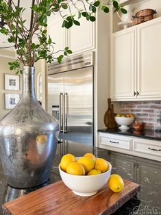 a bowl of lemons sits on a wooden cutting board next to a large metal vase