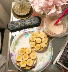 a plate with banana slices on it next to a remote control and pink flower arrangement