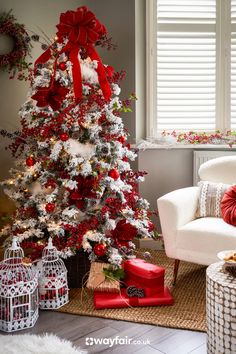 a white christmas tree with red bows and presents in front of the window, surrounded by holiday decorations