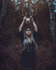 a woman with long hair holding up a deer's skull in front of her face