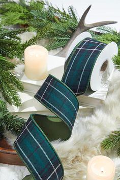 two rolls of green plaid ribbon sitting on top of a table next to evergreen branches