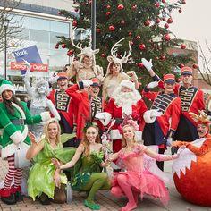 a group of people dressed up in costumes posing for a photo with christmas trees and decorations behind them