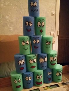 a stack of green and blue toilet paper with faces drawn on them in front of a couch