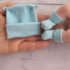 a hand holding a small blue knitted baby hat and booties