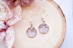 a pair of earrings sitting on top of a piece of wood next to purple flowers