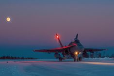 a fighter jet sitting on top of an airport tarmac at night with the moon in the background