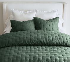 a bed with two pillows on top of it next to a night stand and lamp