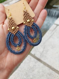 a pair of blue and brown beaded earrings on someone's hand with a tag