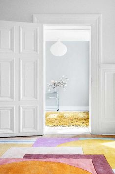 an open door leading to a white room with multicolored rugs on the floor