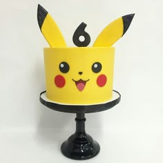 a yellow cake with pikachu ears on it sitting on a black stand against a white background