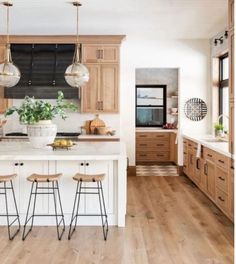 a large kitchen with wooden floors and white counter tops on one side, two hanging lights above the island