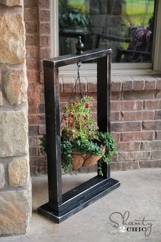 a potted plant hanging from a black frame on the front porch with brick wall