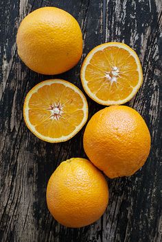 five oranges on a wooden table with one cut in half