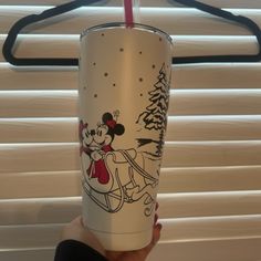 a person holding up a cup with a mickey mouse design on it and a straw in their hand