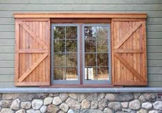 a window with two wooden shutters on the side of a stone wall in front of a house