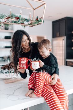 a mother and son sitting on the kitchen counter holding coffee mugs while they look at each other