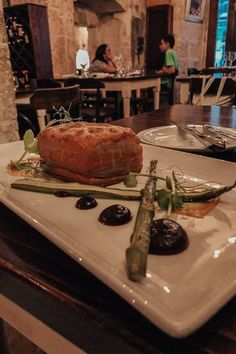 a white plate topped with meat next to asparagus on a wooden table in a restaurant