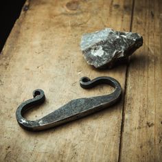 an old metal hook with a rock on the ground next to it and a piece of wood