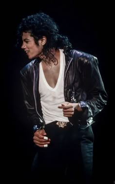 michael jackson performing on stage in the late 1970s or early 1990s, wearing a black leather jacket and white tank top