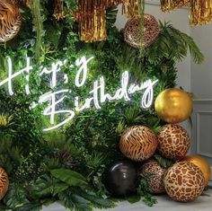 an image of a happy birthday sign surrounded by jungle plants and balloons in front of it