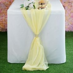 a white table topped with a vase filled with flowers and a yellow cloth draped over it