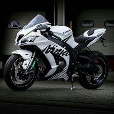 a white and black motorcycle parked in front of a garage door with it's lights on