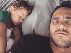 a man laying in bed next to a little boy sleeping on top of his stomach