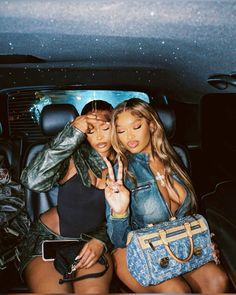 two women sitting in the back seat of a car, one holding her hand up