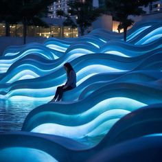 a woman sitting on the edge of a water feature in a city park at night