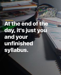 someone sitting at a desk with a book and pen in their hand, next to a pile of books