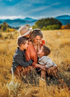 a woman and two boys are sitting in the tall grass with mountains in the background