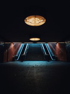 an empty escalator in a dark room with lights on the ceiling and stairs leading up to it