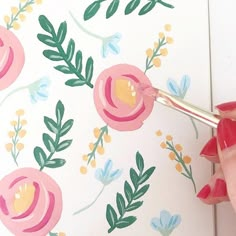 a woman is painting flowers on a wall with paintbrushes and watercolors