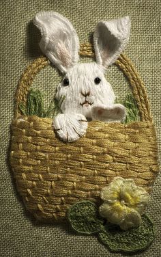 a white rabbit sitting in a basket with flowers on the side and green leaves around it