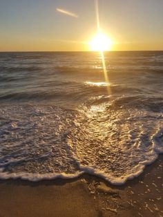 the sun is setting over the ocean with waves coming in to shore and sand on the beach