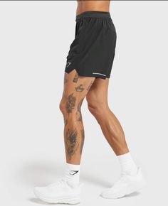 a man in black shorts and white socks with tattoos on his legs, standing against a gray background